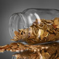 coins spilling from a money jar on gray background
