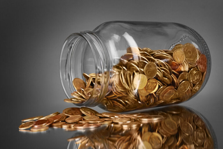 coins spilling from a money jar on gray background